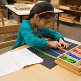 The Gladwyne Montessori School Photo #3 - An elementary student practices math on her own using a hands-on activity for a more in-depth understanding of the concept.